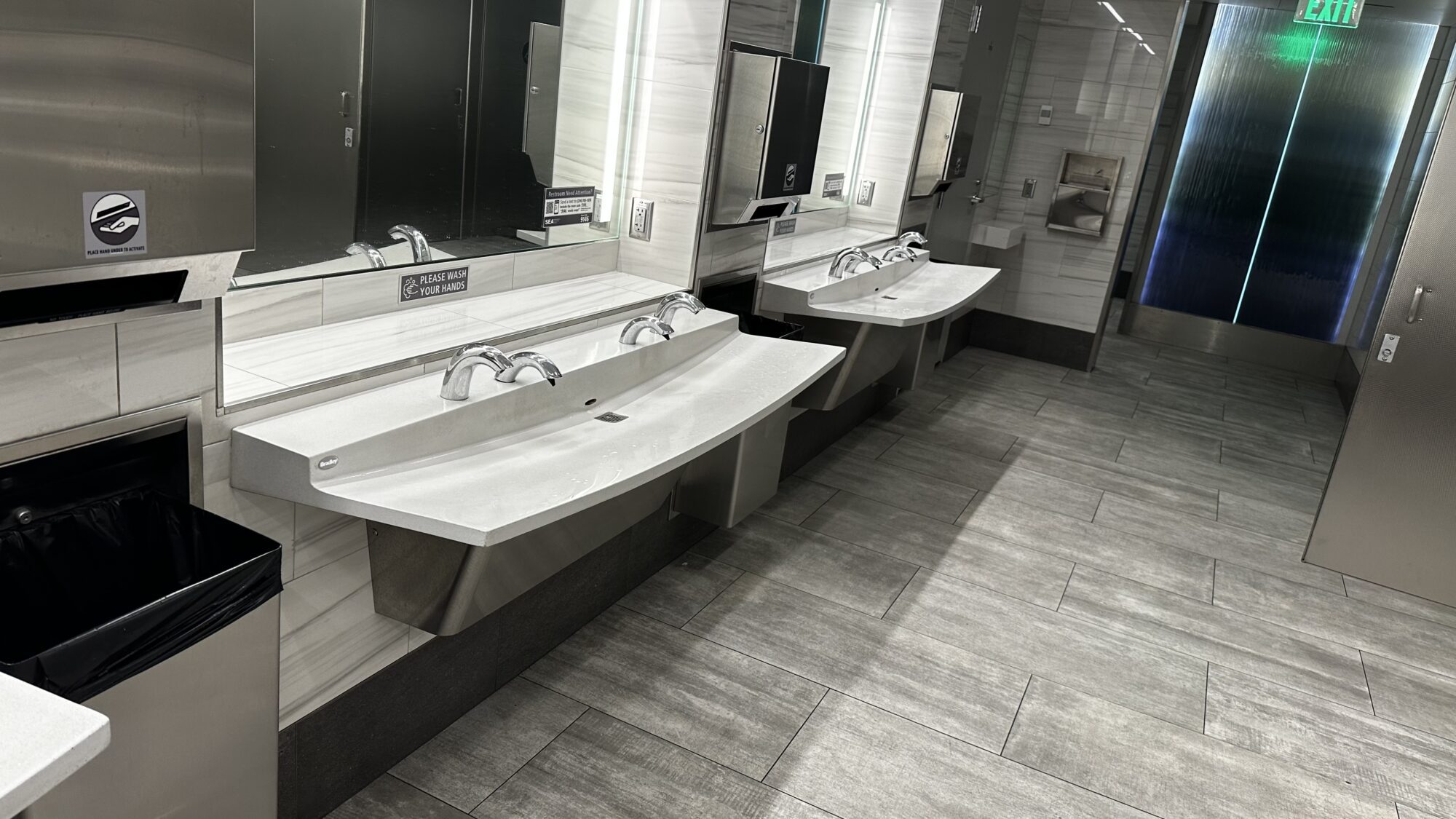 Commercial airport washroom with multiple integrated lavatory basins and chrome faucet installations